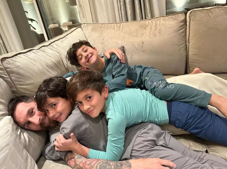 Lionel Messi posa abraçdo com os três filhos, em casa