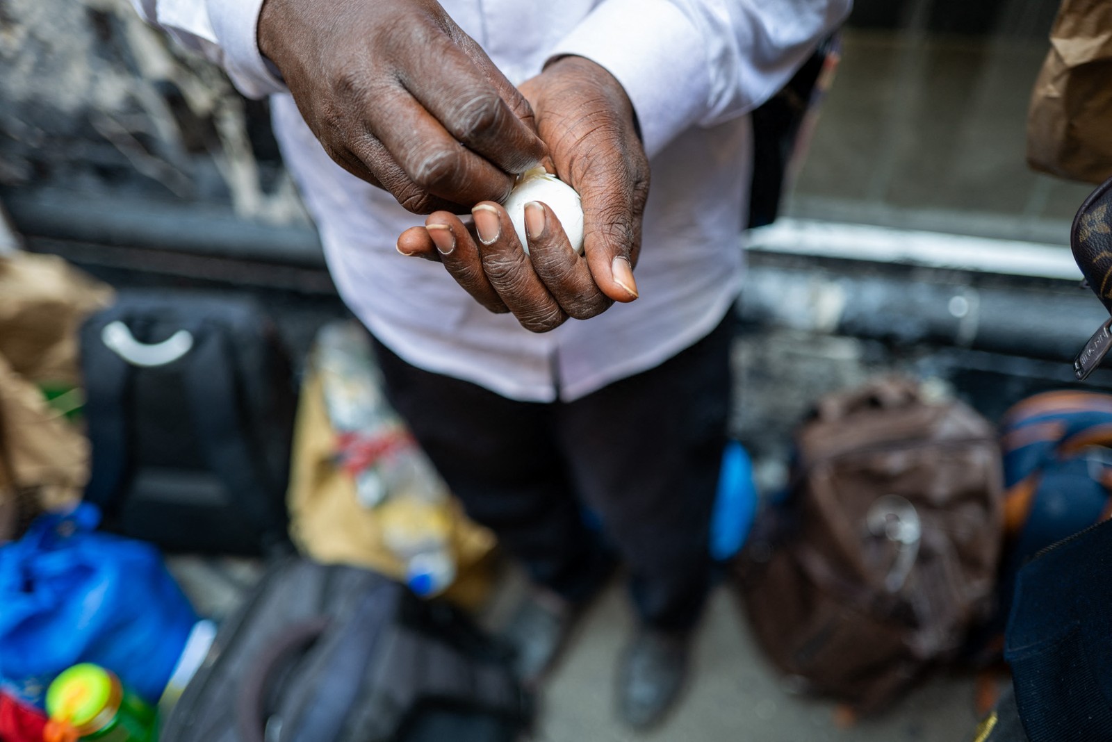 Imigrante do Senegal descasca um ovo enquanto se junta a centenas de outros recém-chegados a Nova York — Foto: SPENCER PLATT / Getty Images via AFP