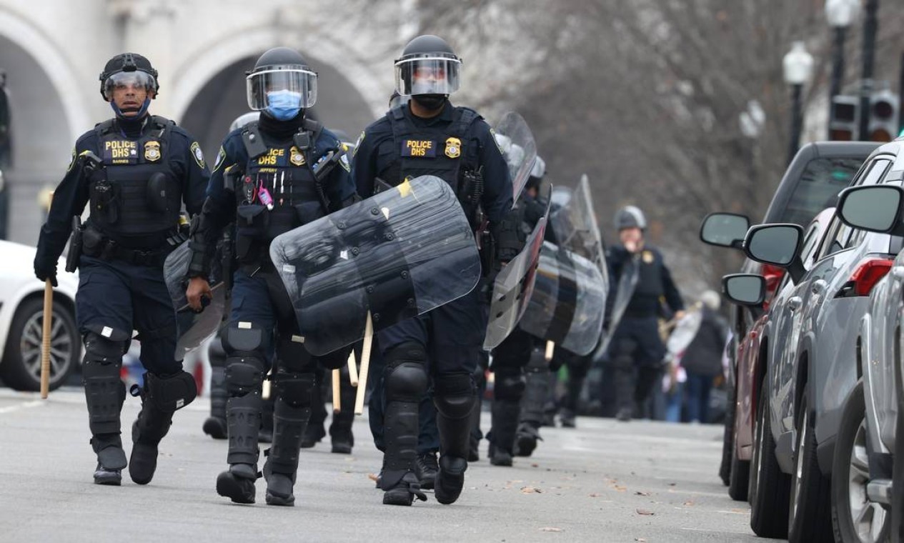 Policiais em traje antimotim caminham em direção ao Capitólio dos EUA enquanto os manifestantes invadem o prédio  — Foto: TASOS KATOPODIS / AFP