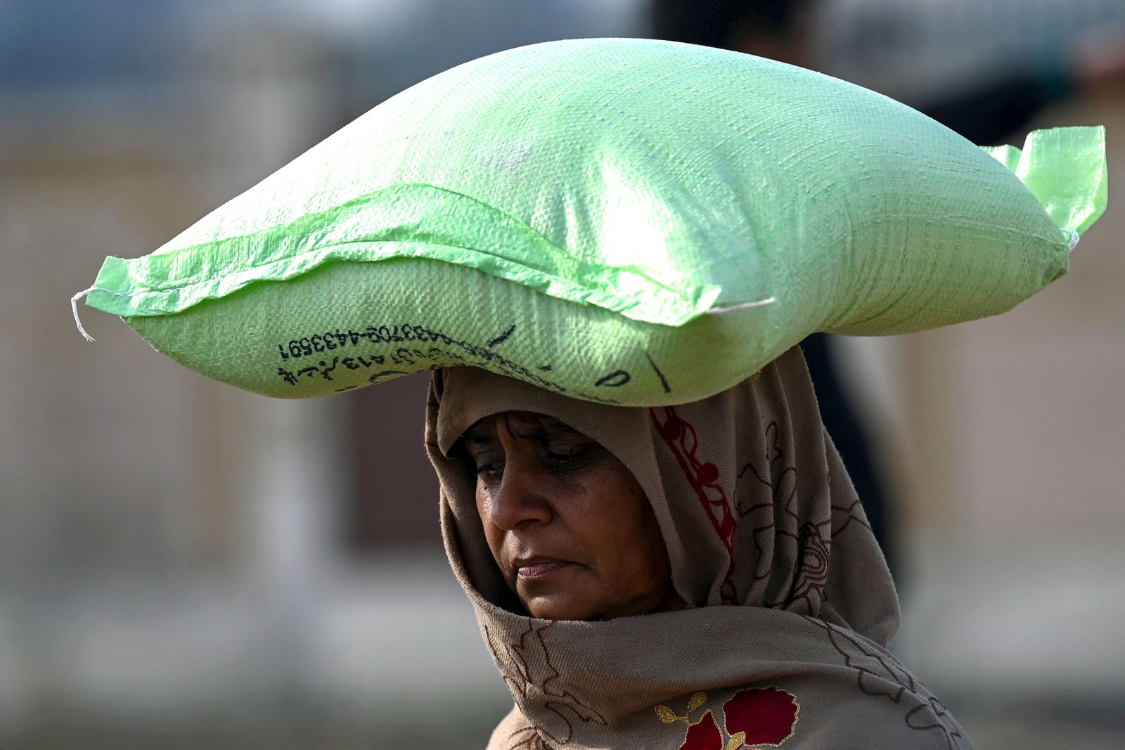 Mulher carrega um saco de farinha de trigo depois de comprar a preços controlados pelo governo em Islamabad, Paquistão — Foto: Aamir QURESHI / AFP