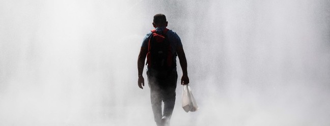 Homem atravessa um spray de água em frente à estação de trem Praterstern, em Viena, em 21 de agosto de 2023, onde a atual onda de calor mantém as temperaturas em torno de 35°C — Foto: Alex HALADA / AFP