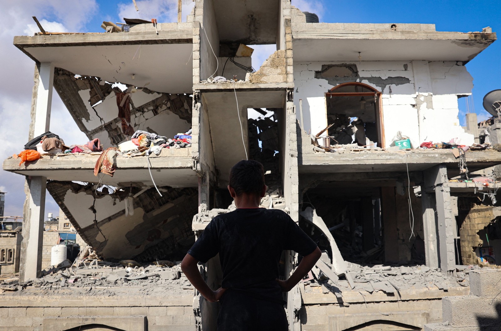 Um jovem palestino em frente a um prédio destruído após o bombardeio israelense no distrito de Tal al-Sultan, em Rafah, no sul da Faixa de Gaza — Foto: AFP