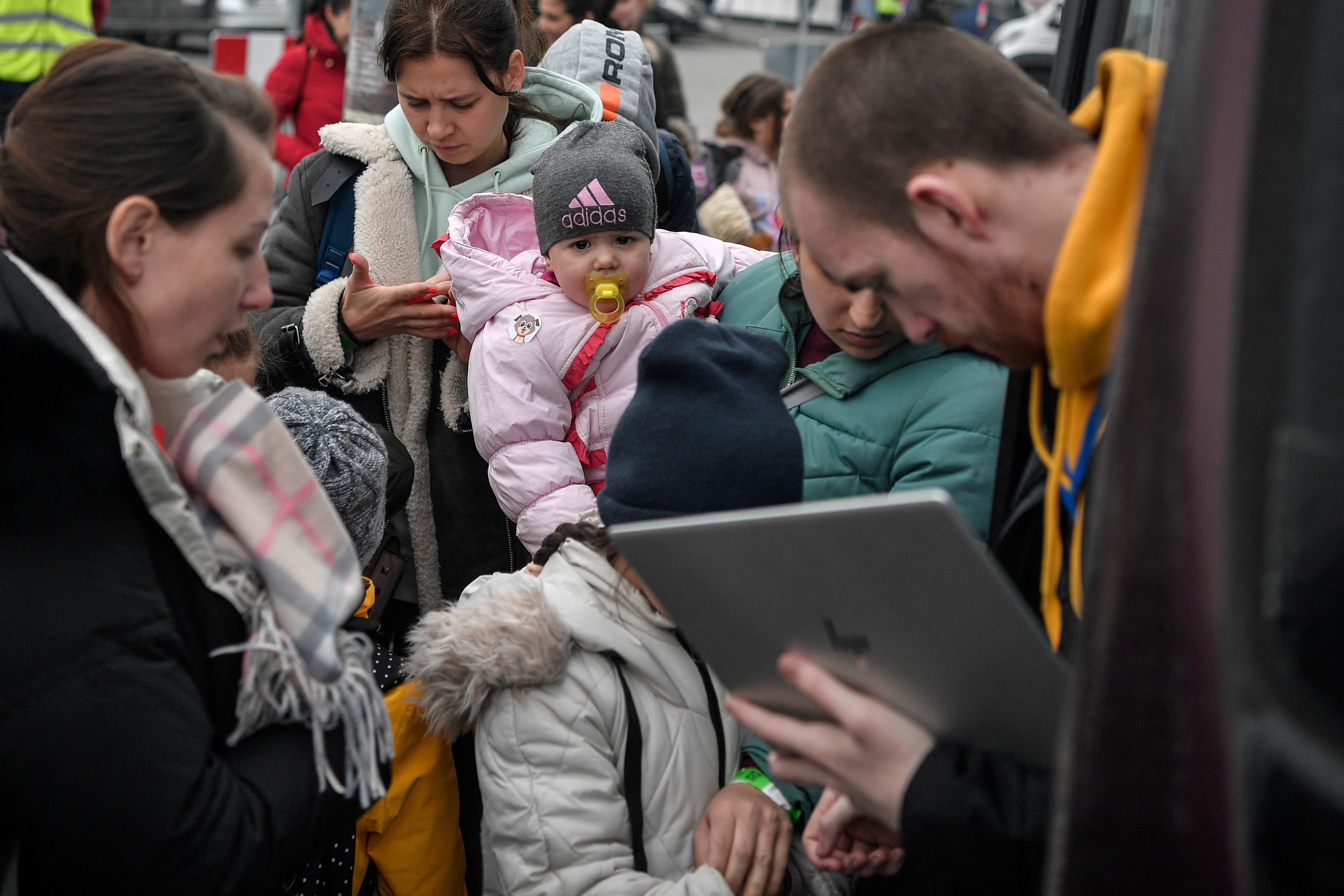 Na Polônia, mulher segura o bebê enquanto homem checa identidades antes do embarque para Portugal
