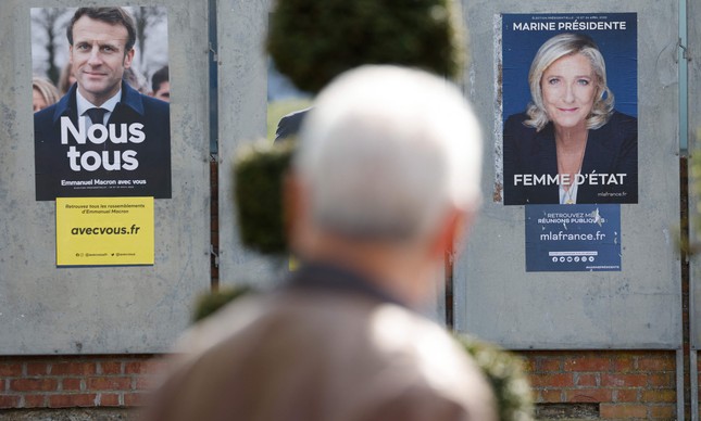 Homem passa por cartazes de campanha dos candidatos presidenciais franceses, o incumbente Emmanuel Macron e a candidata da extrema direita Marine Le Pen em Denain