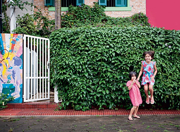 Aurora e Olímpia brincam na rua, em frente ao muro tomado pela tumbérgia. O grafite logo ao lado, feito por Arnaldo Degasperi, pai das meninas, retrata as duas. Repare na divisão das casas geminadas: a parede de tijolinhos é da casa da família (Foto: Gui Morelli/Editora Globo)