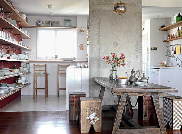 A estante, que começa na cozinha e termina na sala de jantar, guarda, além de louças e copos, livros e objetos de decoração. Ela integra ambientes no apartamento da chef Cris Maccarone. A mesa fica apoiada na coluna estrutural, descoberta na reforma (Foto: Marcelo Magnani/Casa e Jardim)