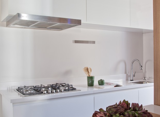 Com a estrutura de instalação escondida dentro do armário, a coifa se mantém discreta sobre o cooktop. As bancadas do ambiente são de silestone branco. Repare que os armários suspensos brilham, enquanto os próximos do piso ganharam acabamento opaco (Foto: Luís Gomes)