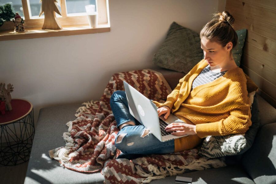 woman in yellow cardigan sitting cross legged working on laptop