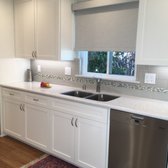 This bright kitchen features white cabinets, silver hardware, and quartz counter tops. A grey tile and mosaic backsplash adds dimension.