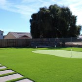 Outdoor living space feauturing a prutting green, artificial turf, a paver walkway, raised paver patio, and a fire pit.