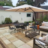 This beautiful golden stone tile patio is surrounded by potted plants, some natural landscaped borders with bamboo, raised beds and vines.