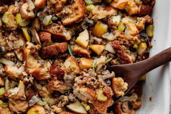 sausage herb Thanksgiving stuffing in a white baking dish with wooden spoon.