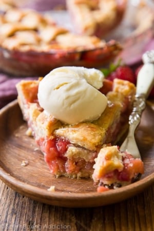 slice of strawberry rhubarb pie with a scoop of ice cream on a wood plate with a fork