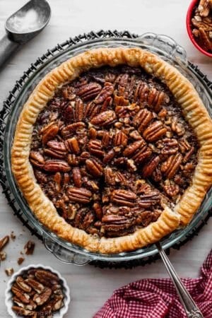 pecan pie in glass pie dish with slice already cut and about to be taken out with pie server.