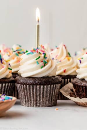 chocolate cupcakes with vanilla buttercream, rainbow sprinkles, and a gold birthday candle.