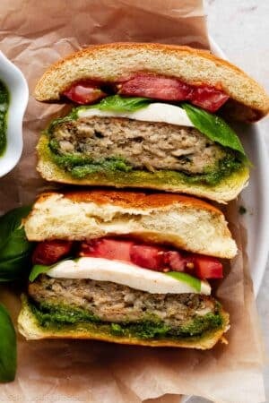 caprese pesto chicken burger with tomato and basil cut in half and face up.