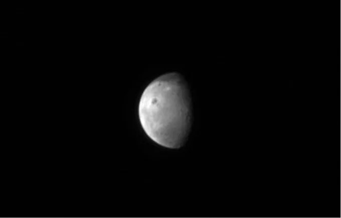 The black background of space contrasts with the white-grey color of the moon. The moon rests in the center seeming to float peacefully in space. About sixty percent of the moon is illuminated by the sun showing some of the larger craters that darken the moon’s surface.