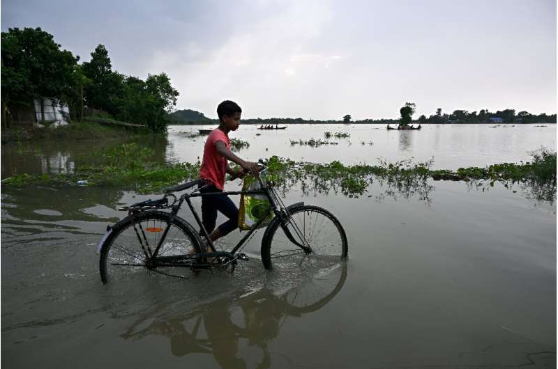 A boy pushes his bicycle through a flooded part of Jhargaon village in Morigaon district, Assam