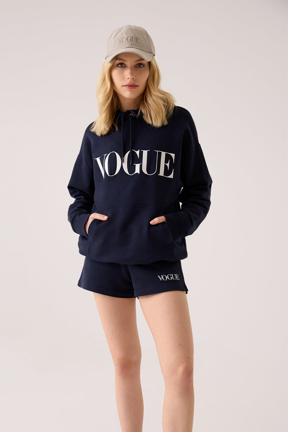 Model frontal stehend trägt den gesamten VOGUE Loungewear-Look: VOGUE Hoodie in Navy mit passender kurzer Sweatpants in Navy