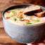 Bowl of soup with two slices of bread on top being held