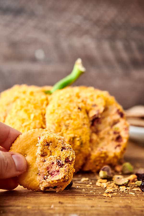 scoop of cheese on a cracker with pumpkin cheese ball in the back