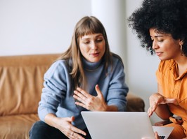 Two young businesswomen having a discussion while looking at a laptop screen. Two female entrepreneurs working as a team in a modern workplace.