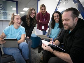 Four women and a man take notes and laugh during a meeting.