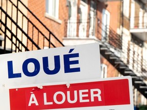 Closeup of a for rent sign with red brick townhouses blurred in the background.