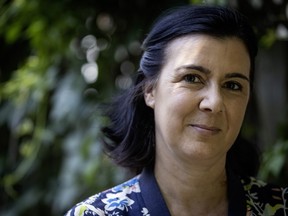 A woman half-smiles at the camera, with greenery in the background.