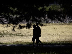A couple in silhouette walk past trees in a park.