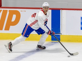 Michael Hage, in a white jersey and blue hockey pants, has the puck on his stick as he skates past a blue line.