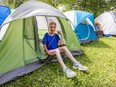 A woman sits in the entrance of a tent in an encampment in a park.