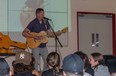 Nathan Crawford stands in front of a crowd of sitting students while playing the guitar.