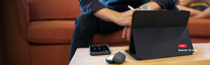 An iPad in a Balance Folio case sits on a table in view stand formation with a man on a couch in the background.