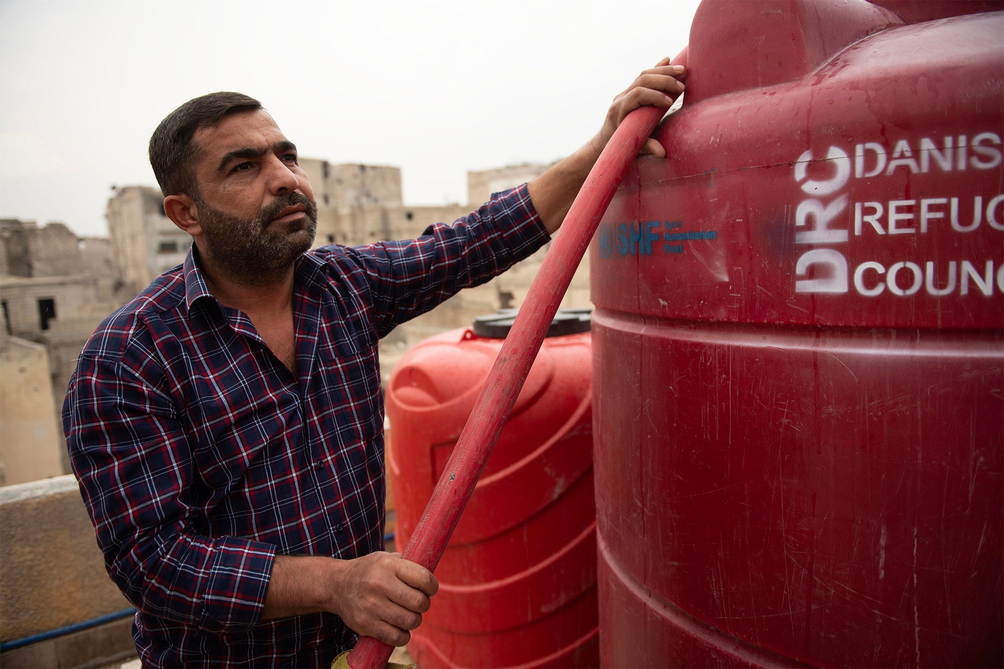 Kamel*, pictured helping aid workers in Aleppo, was supported by the water programme from DEC charity Oxfam. He lives in a shelter with Mounir*