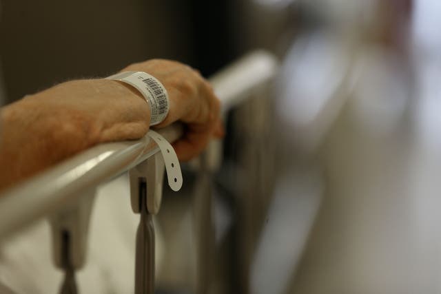 <p>A patient clutches the bars of his hospital bed</p>