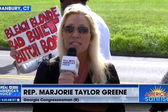 <p>Majorie Taylor Greene speaks outside a Danbury, Connecticut, prison as Steve Bannon turns himself in. A protestor held up a sign mocking the Georgia representative during her TV appearance  </p>