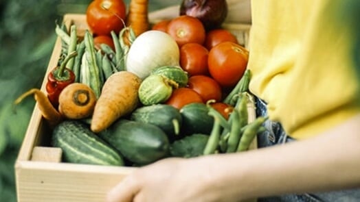 Person carrying a wooden box full of fresh vegetables