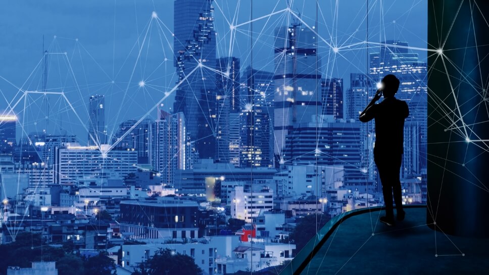 Man looking out a big window at an evening cityscape