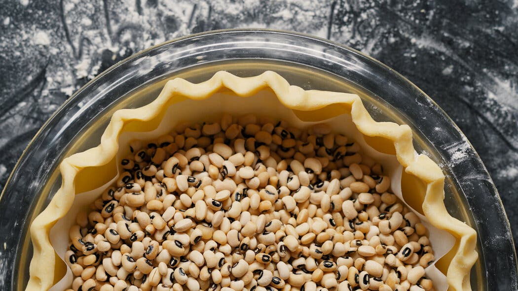 Image of a pie crust weighed down with parchment and dried beans, prepared to be par baked.