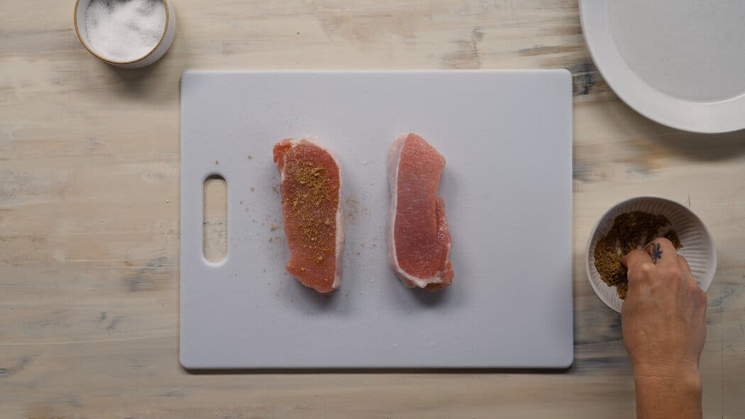 Image of two raw pork chops being seasoned with a spice mixture for making air-fryer pork chops.