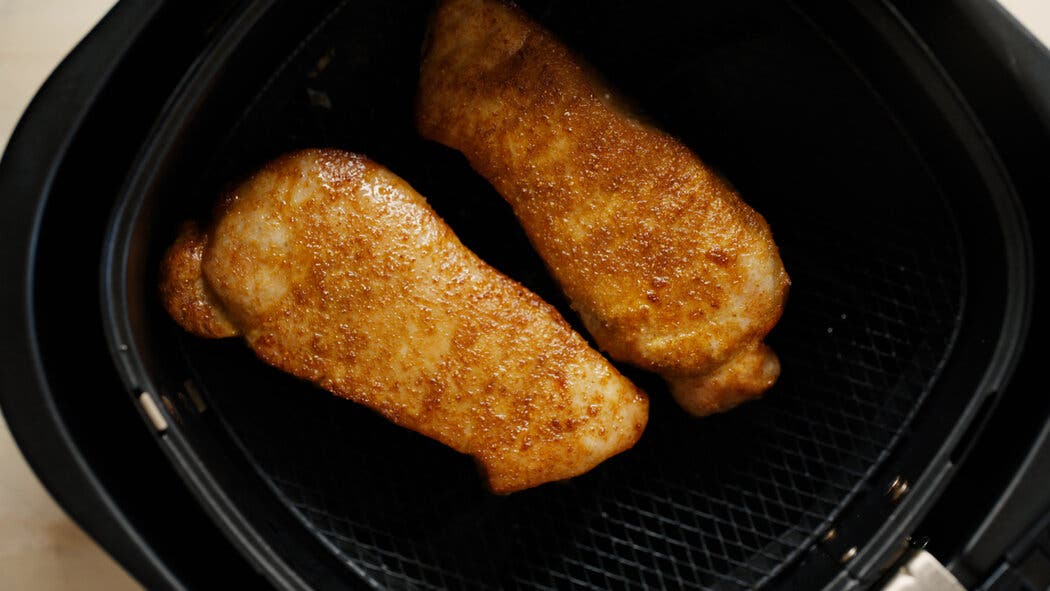 Image of golden brown pork chops in an air-fryer basket for making air-fryer pork chops.