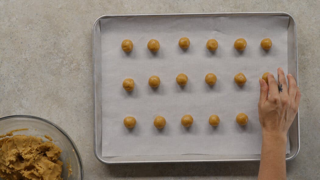 Image of dough being formed into small balls and placed on a sheet tray for making Peanut Butter Blossoms