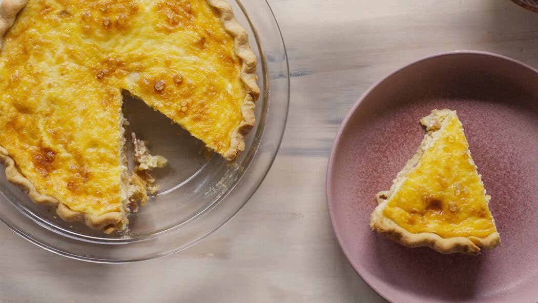 Image of baked quiche with a slice taken out and placed on a plate for making a Quiche Lorraine.