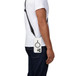 Tech21 Crossbody Flex Quartz case, attached to strap with iPhone inserted, hanging on side of a person in white shirt and jeans