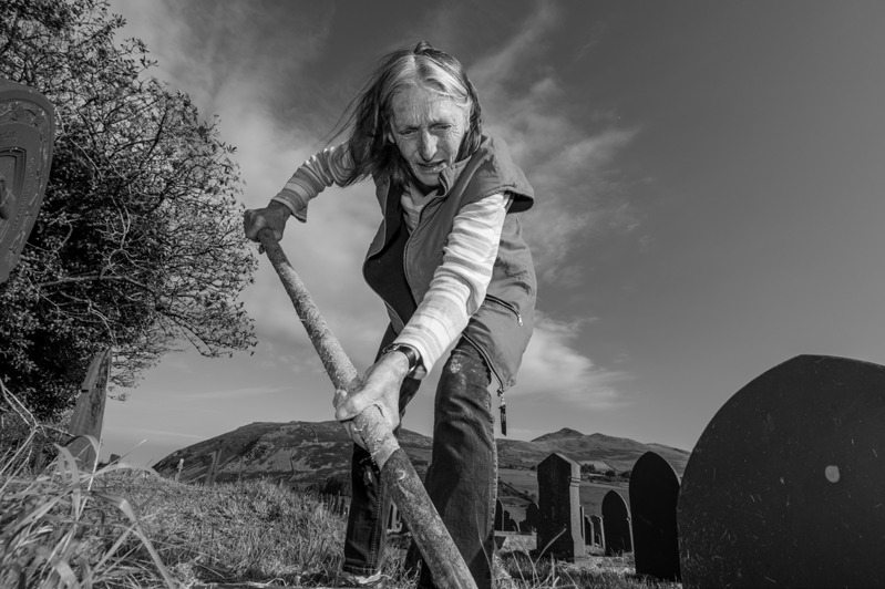 In her eightieth year Olwen was carrying out physically demanding work clearing graves. She is seen hear turning over vegetation in the gravel at the cemetery in Llanaelhaearn on the Llŷn Peninsula.