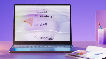 Laptop displaying the words Co-author, Co-assist, Co-produce, Co-draft, and Co-innovate to convey Copilot's capabilities on a purple background, with a pen holder and a notebook on the desk