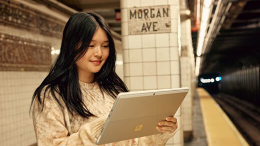 Una mujer mira su Surface Pro dispositivo mientras está en una plataforma subterránea del metro.