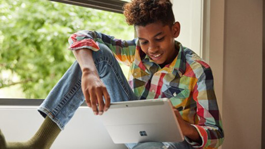 Un joven estudiante sentado en una ventana mirando su dispositivo Surface Pro.