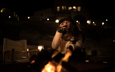 woman at night by a fireplace drinking wine